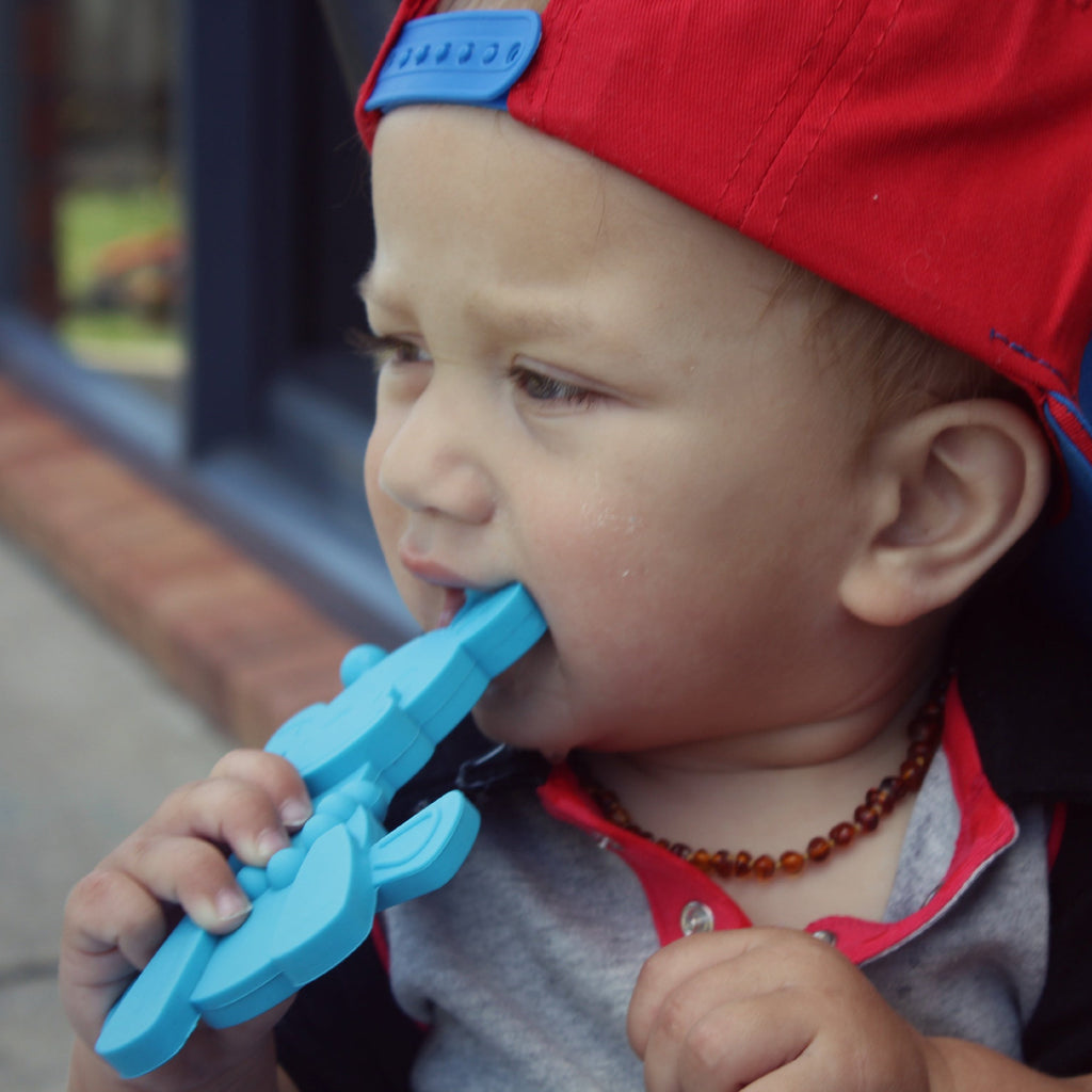 Baby gripping a cyan giraffe-shaped teething toy for chewing