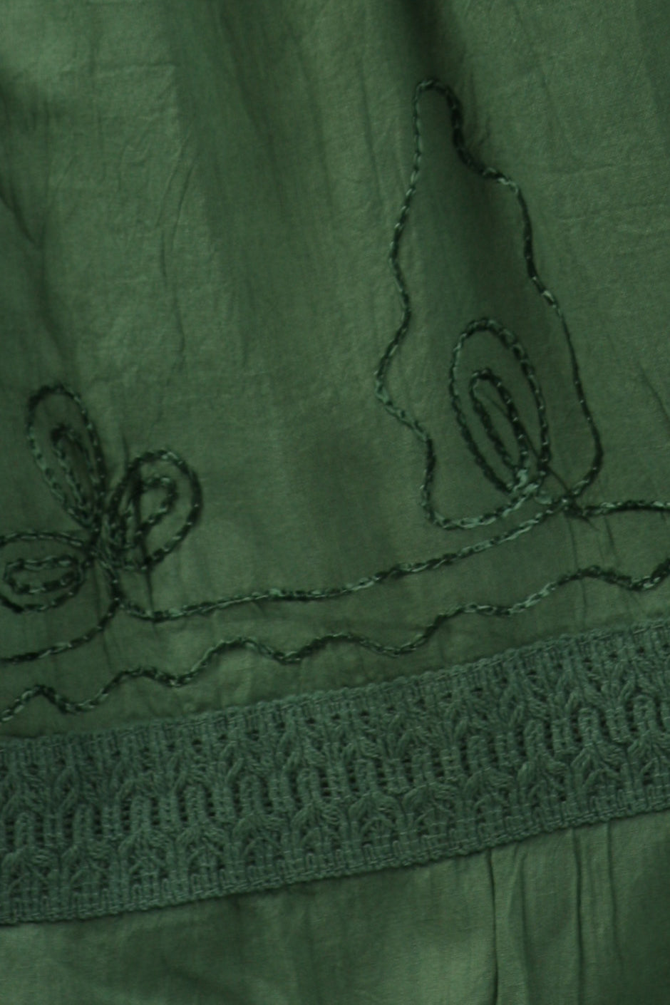 Close-up of green fabric with floral embroidery, contrast stitching, and tiered bands