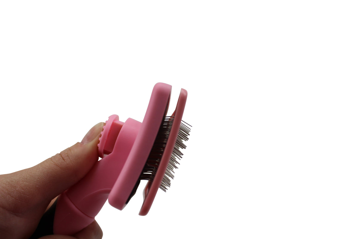 Hand-held self-cleaning pet slicker brush close-up with steel bristles and pink slide cleaner