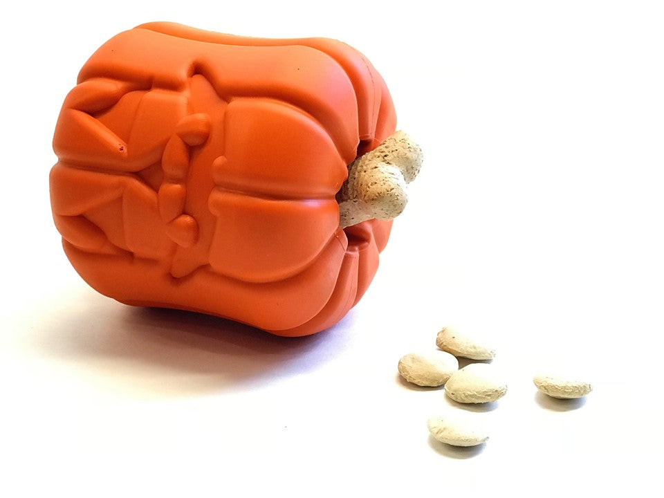 Orange jack-o'-lantern dog treat dispenser toy with rubber texture and treats beside it.