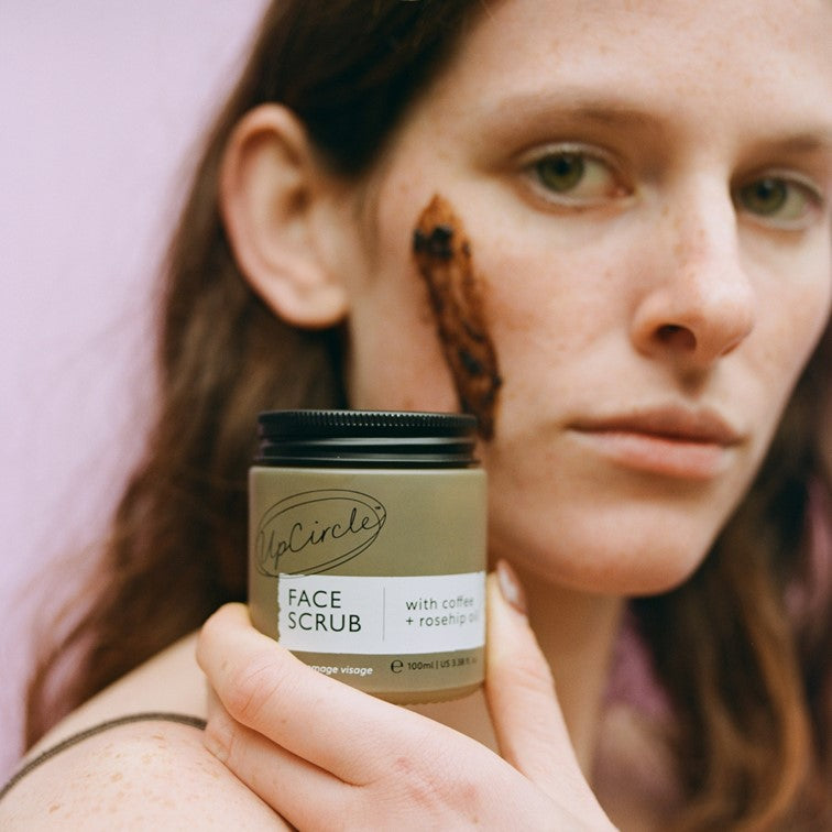 Face scrub jar with coffee and rosehip oil, beige label, held by hand