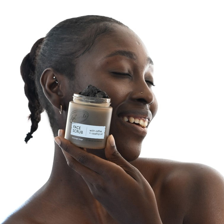 Woman holding face scrub jar near face with eyes closed and smiling