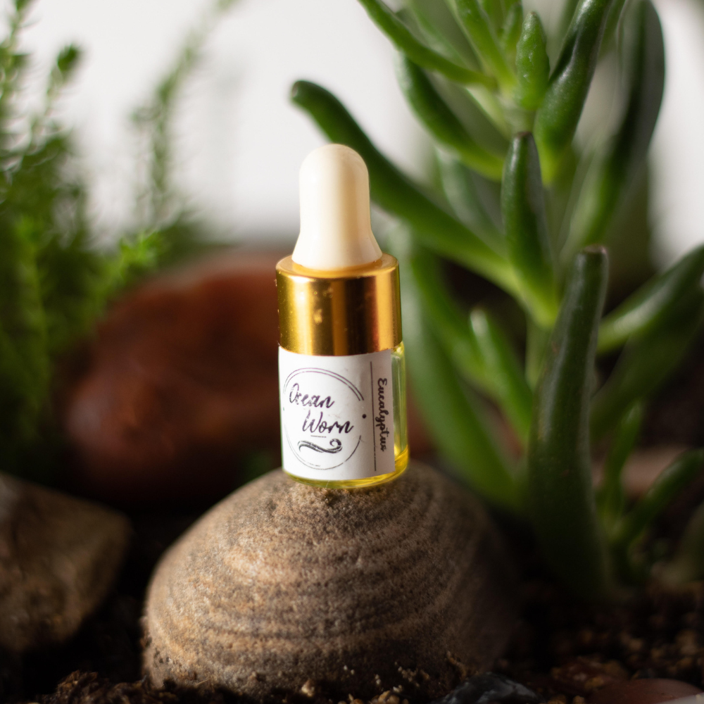 Gold-capped essential oil bottle on textured stone base with green leaves