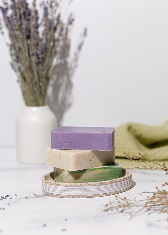 Cold-processed soap bar stack: purple top, beige and light green bars.
