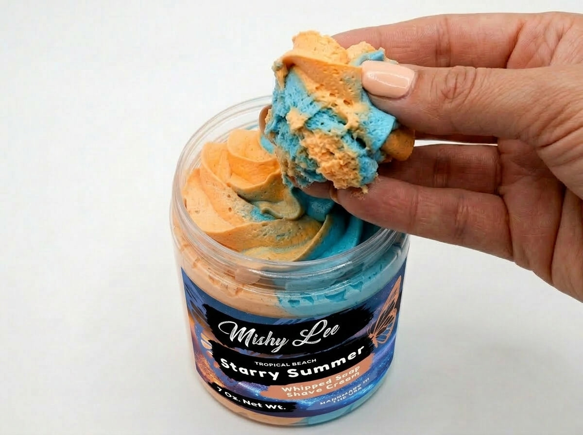 Hand holding peach-and-blue whipped cream scoop above open whipped soap jar