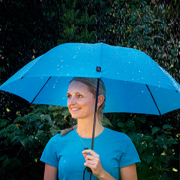 Blue trekking umbrella with dome-shaped canopy and center shaft, open in rain