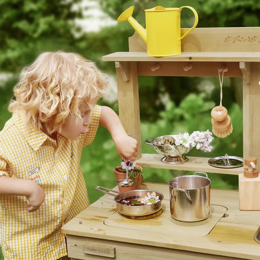 Kids cooking at outdoor wooden mud kitchen playset with pots and hanging tool clips