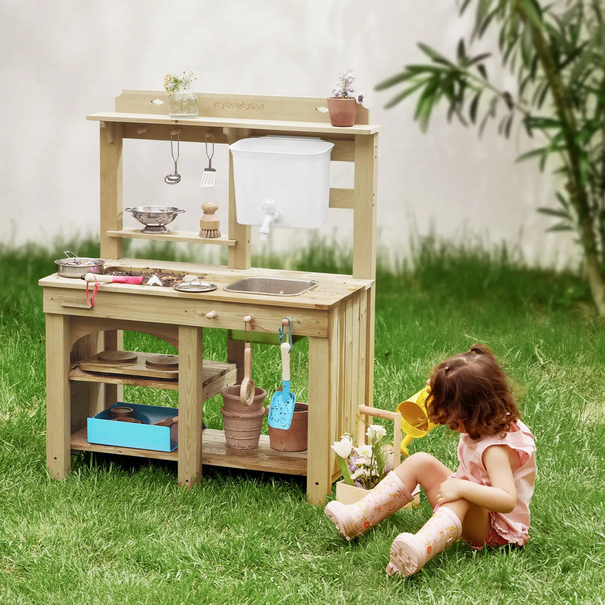 Kids beside outdoor wooden mud kitchen playset with storage shelves and water spout