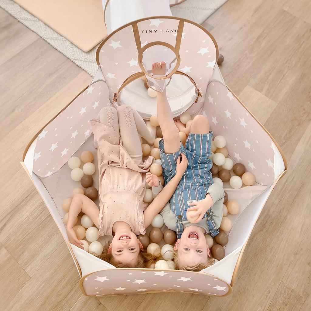 Star fabric play tunnel with open entrance and foam balls, two children inside, beige and white