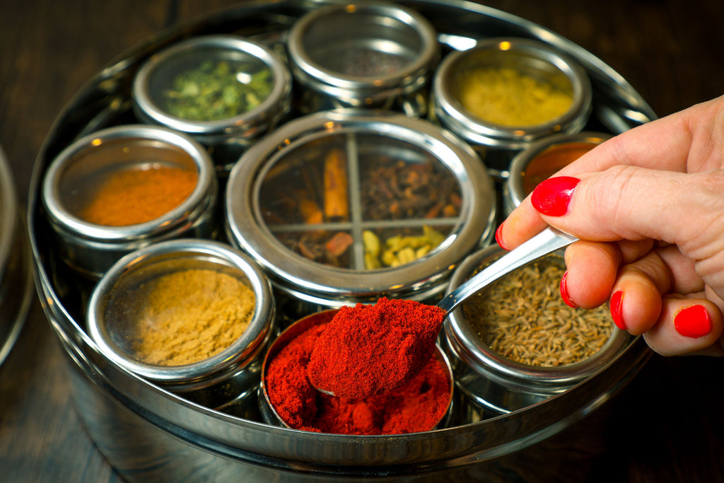 Stainless spice wheel with multiple round wells; hand sprinkles red spice powder