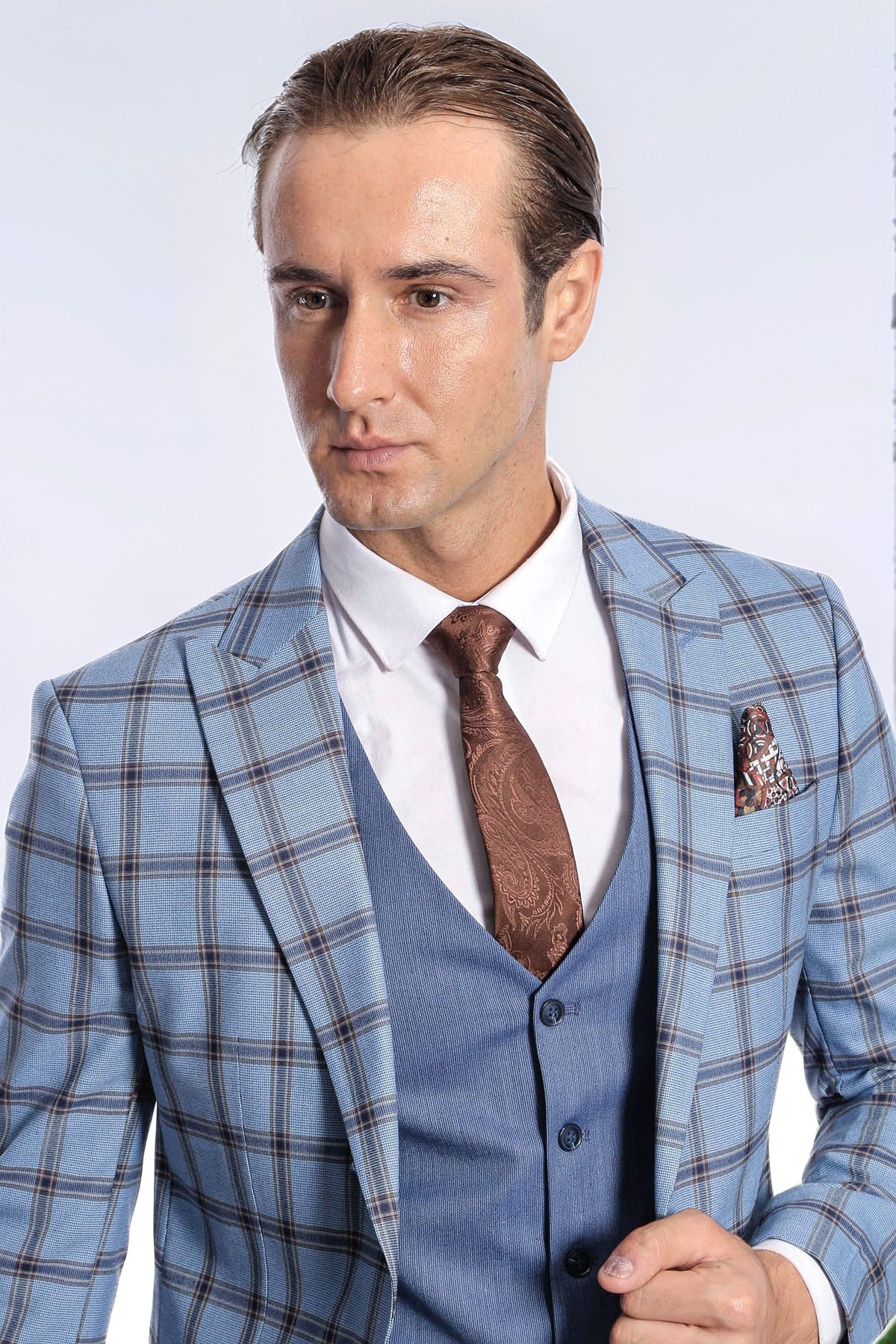 Men's slim fit plaid suit jacket close-up with blue vest, brown tie, and patterned pocket square