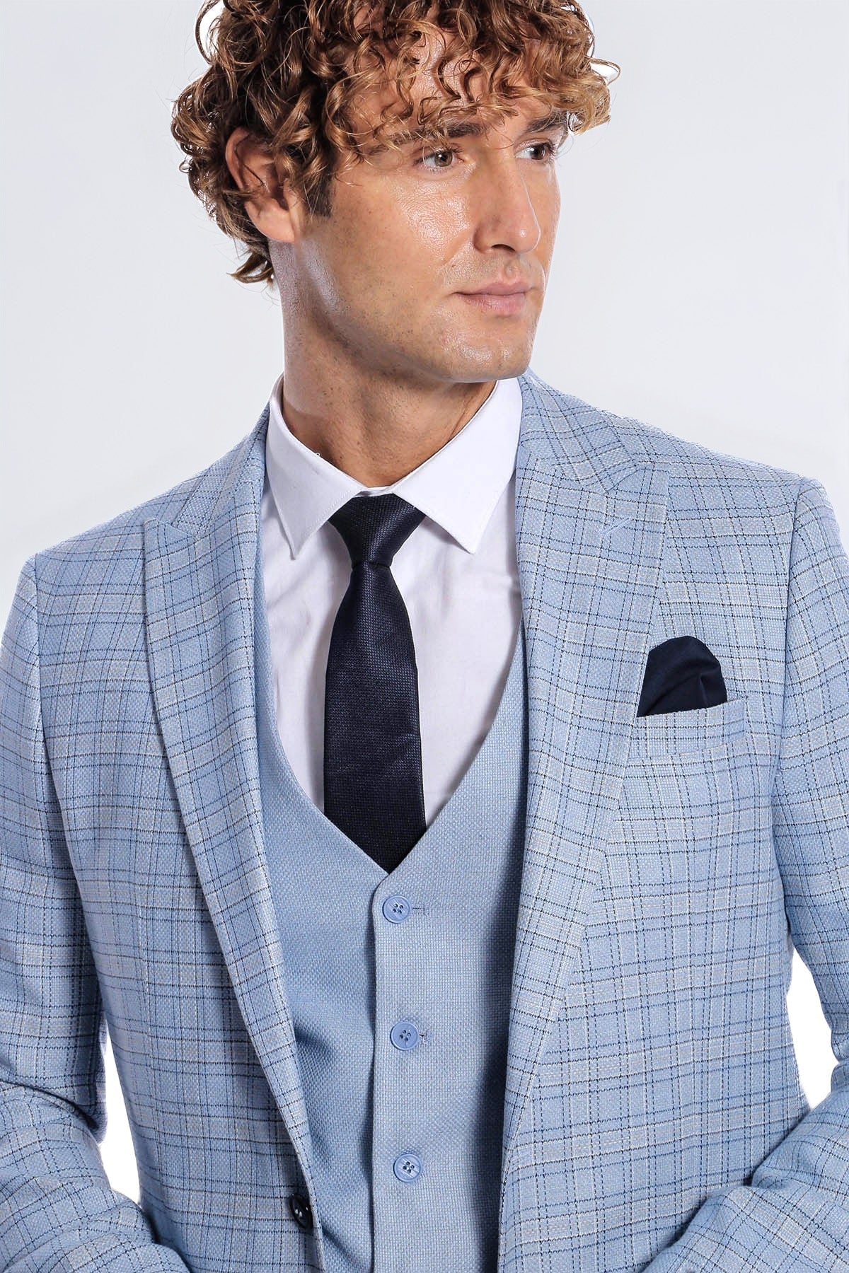 Light blue checked suit jacket with black tie, light vest, and pocket square.