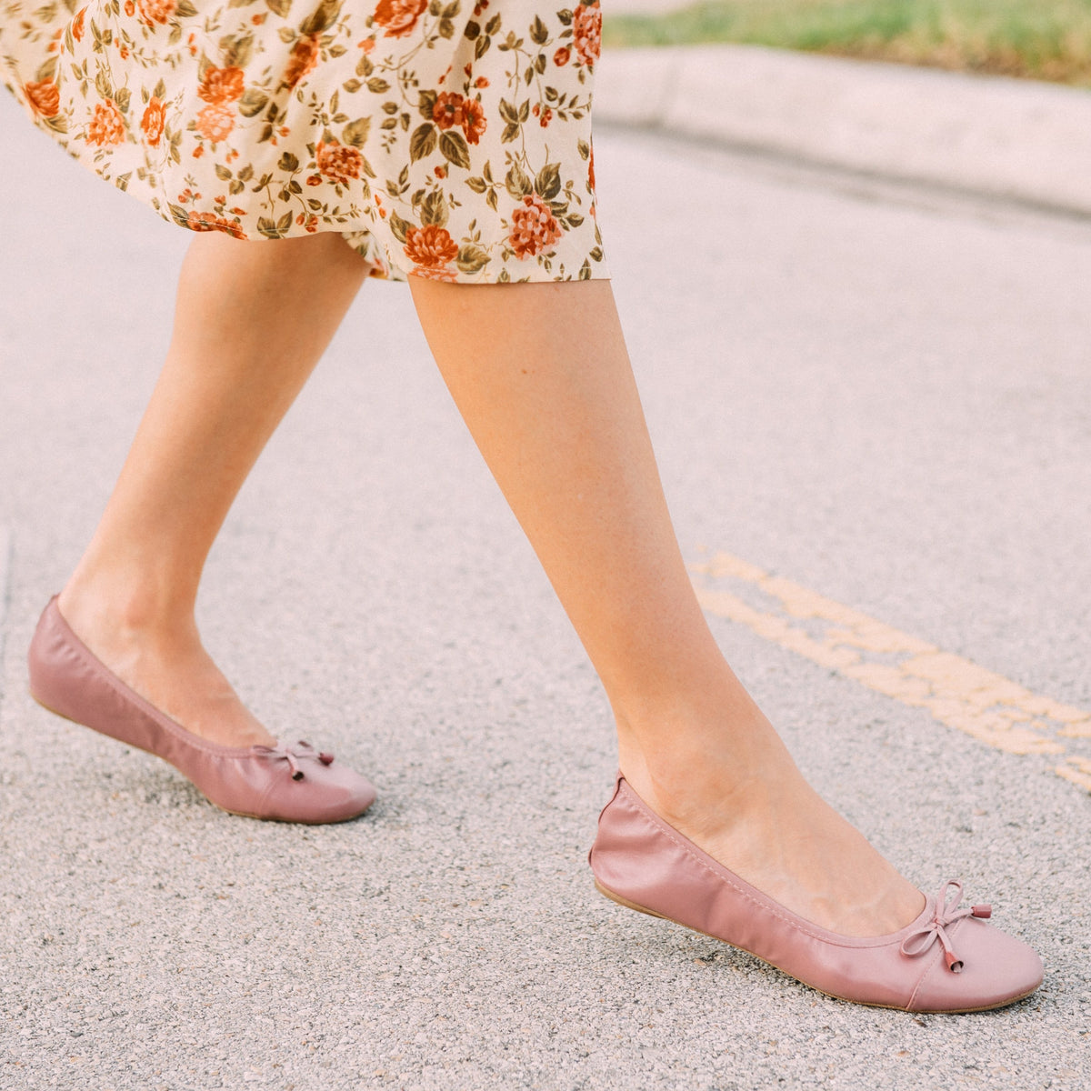 Dusty rose flats with bow ties stepping forward on pavement, rounded toe
