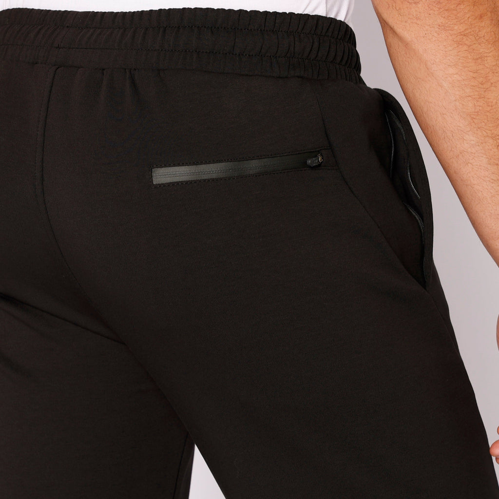 Black sweatpants detail: elastic waistband and zip pocket on front leg.