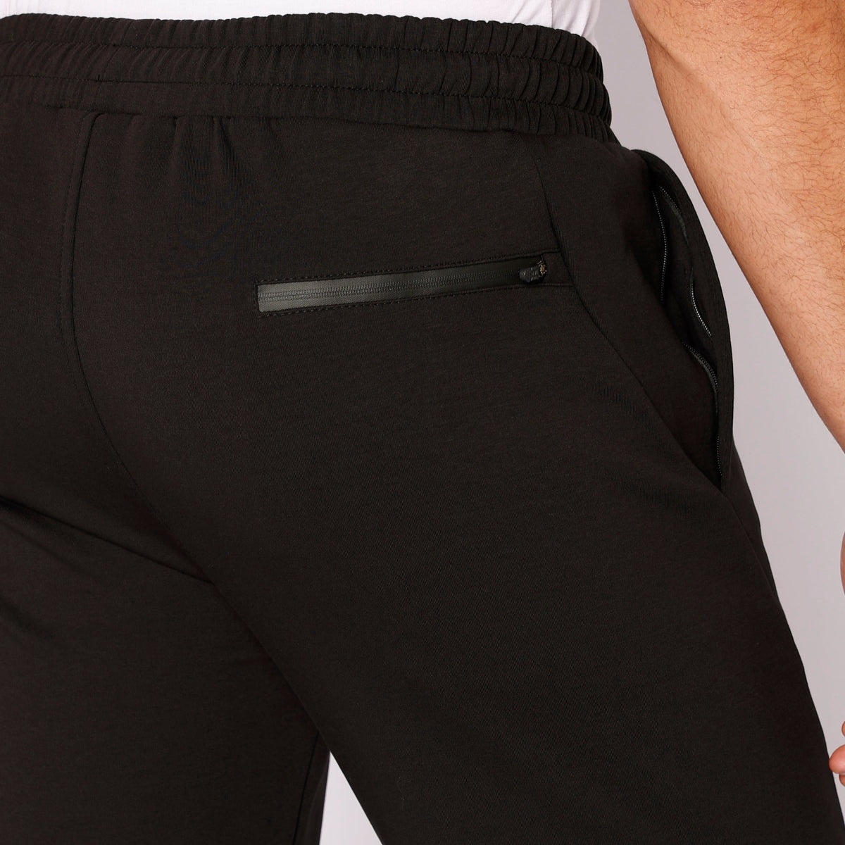 Black sweatpants detail: elastic waistband and zip pocket on front leg.