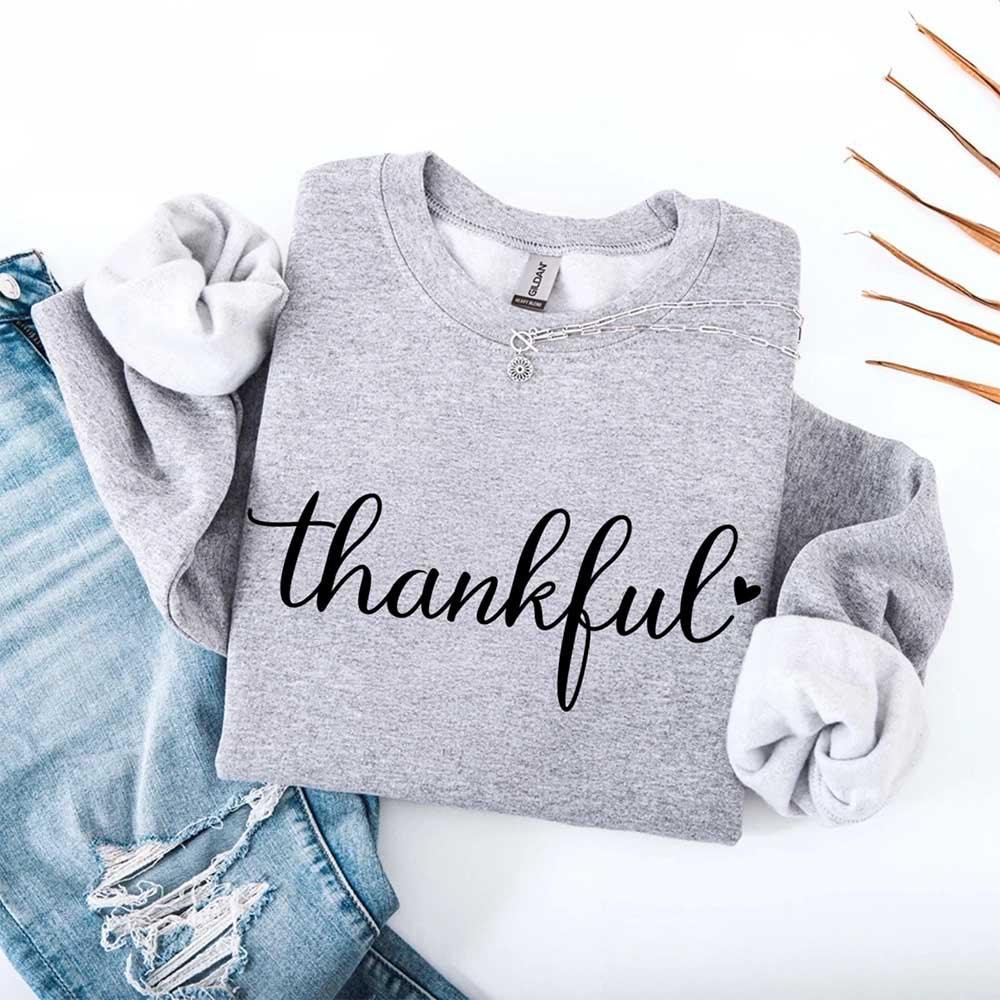 Light gray crewneck sweatshirt with “thankful” script print and chain charm detail at neckline