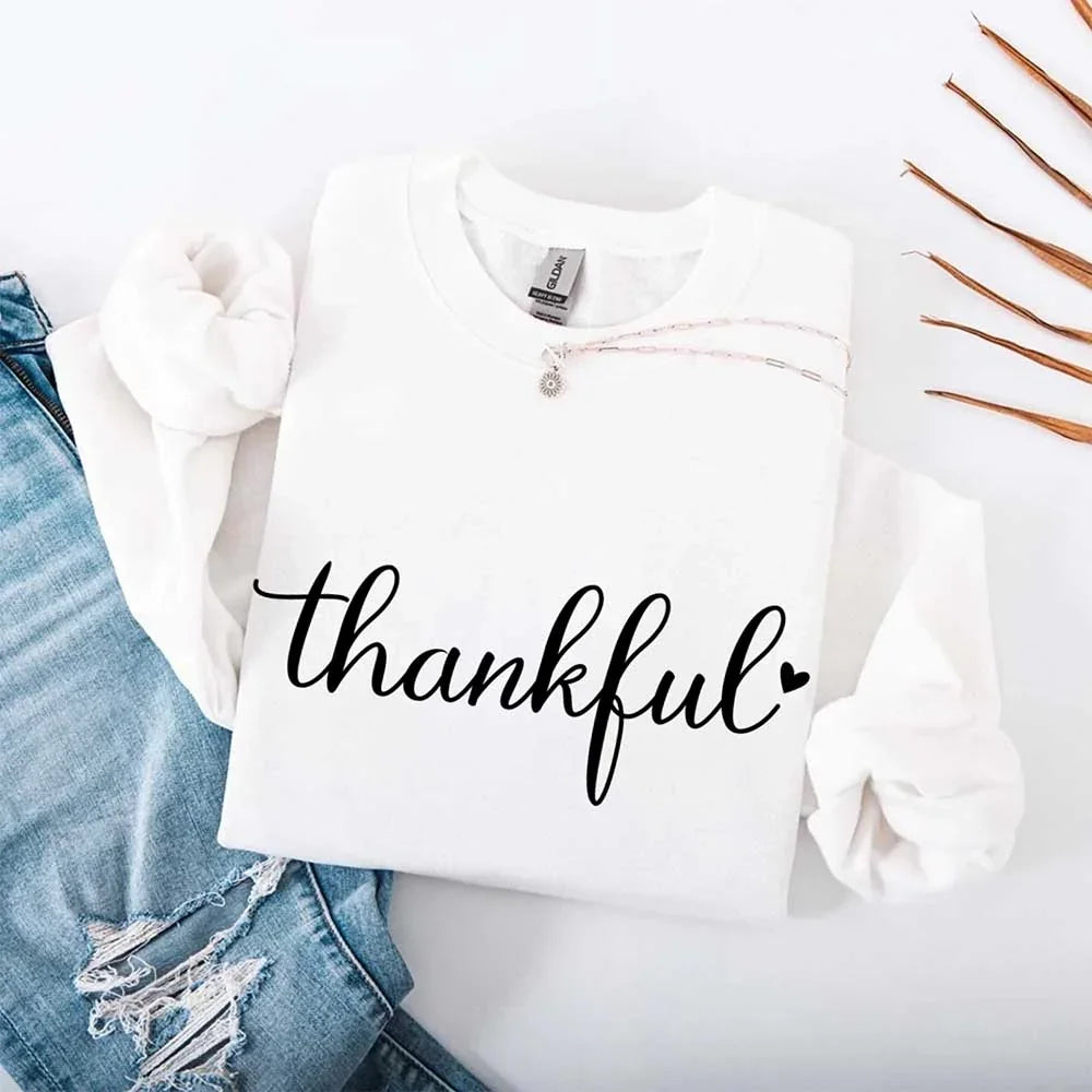 White crewneck sweatshirt with “thankful” script print and necklace charm detail at neckline