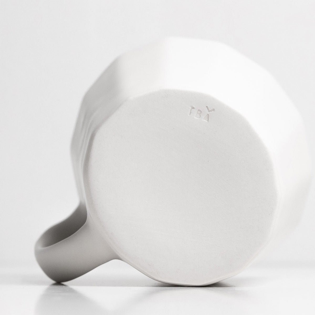 Handmade porcelain coffee mug base, matte white underside with small maker mark