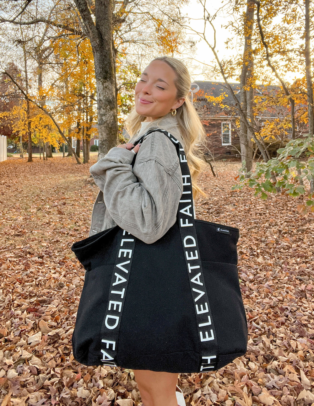 Black tote bag with long handles and vertical white 'ELEVATED FAITH' print on front.