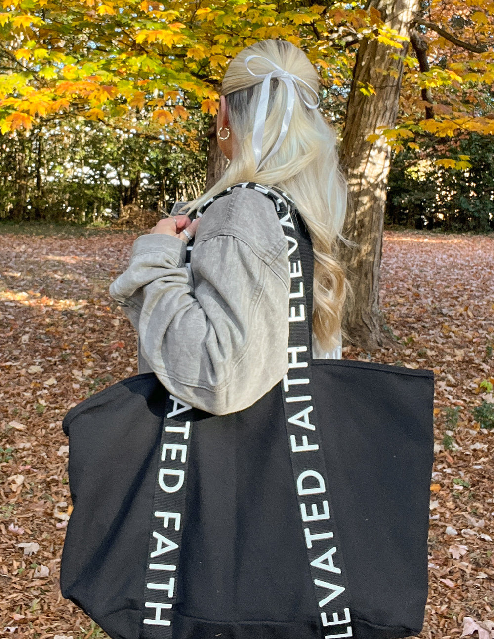 Black tote bag with long handles and vertical white 'FAITH' lettering on strap.