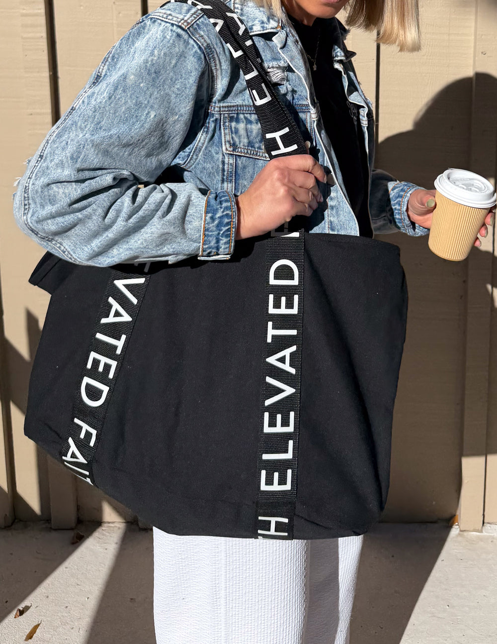 Black tote bag with long handles and vertical white logo lettering on front.