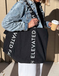 Black tote bag with long handles and vertical white logo lettering on front.
