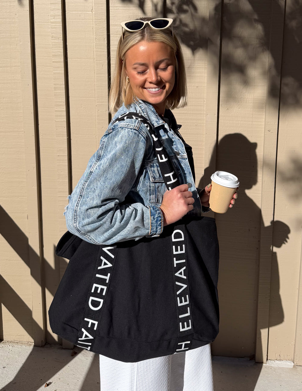 Black large tote bag with long handles and vertical white 'ELEVATED FAITH' lettering.