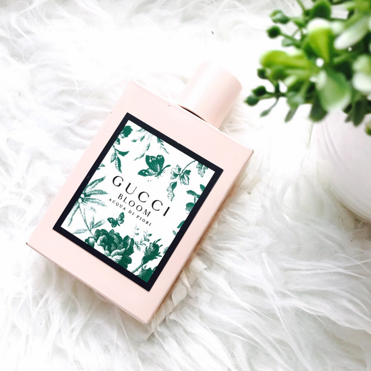 Pink perfume bottle angled on white fabric, Gucci Bloom green floral label