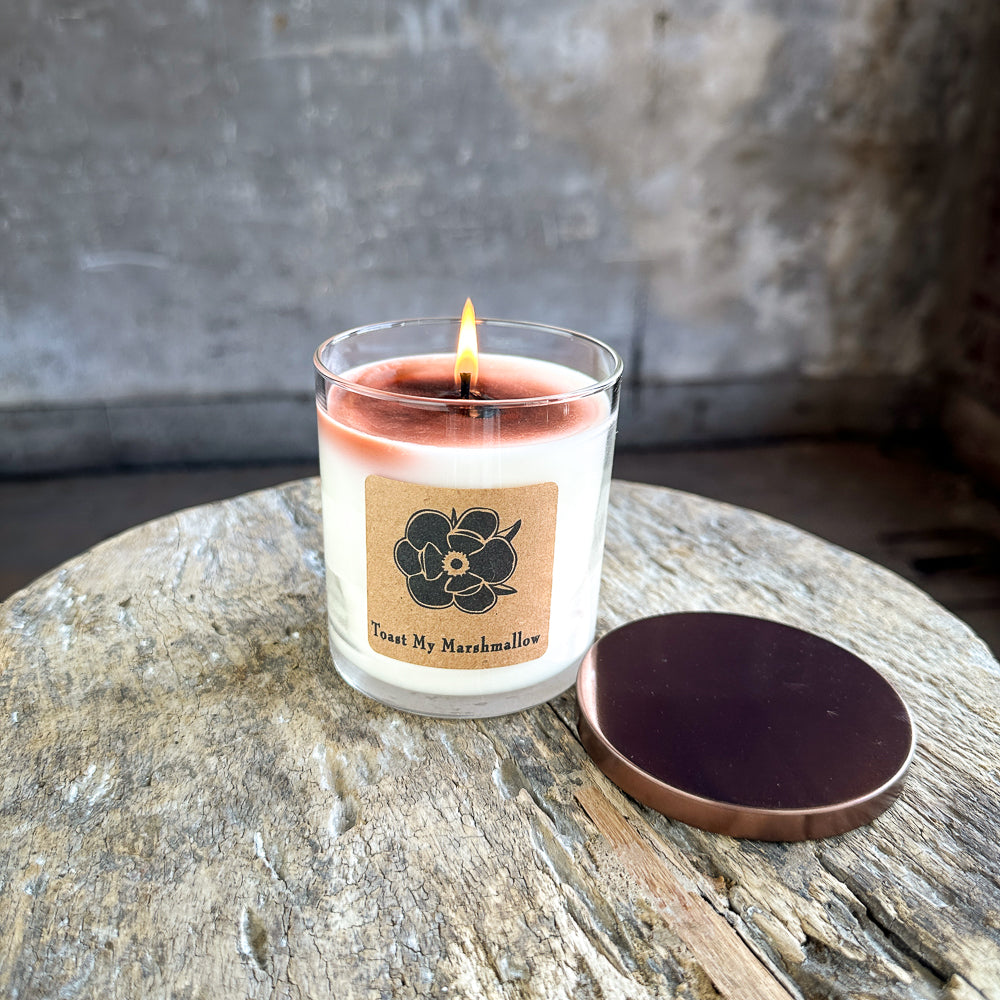 Burning soy candle in clear glass jar, cream wax and floral label, lid off