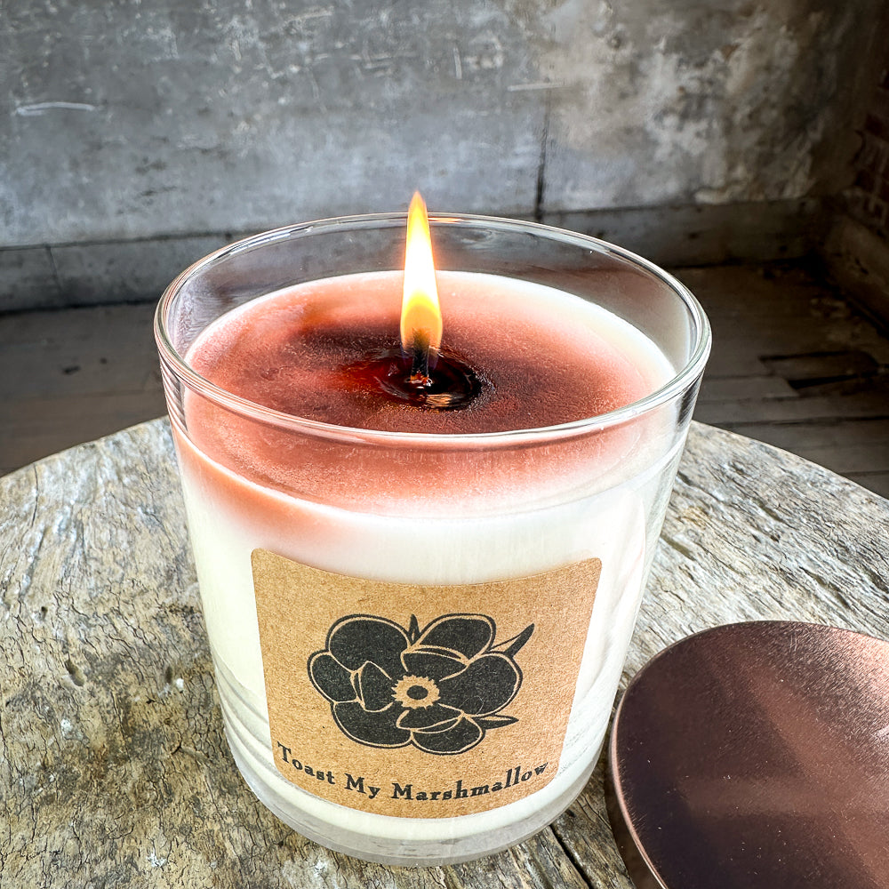 Burning soy candle close-up in clear glass jar, cream wax with warm glow and label