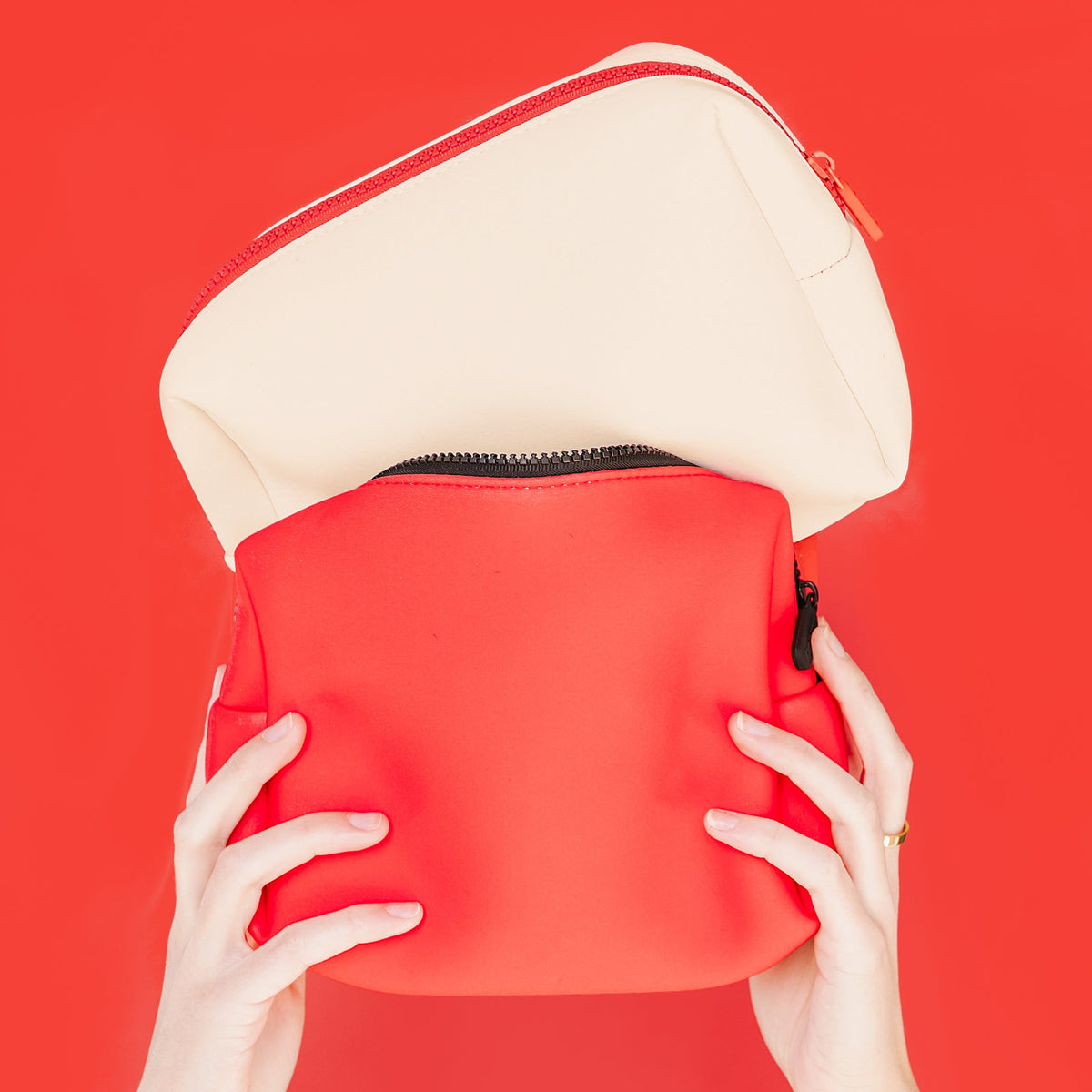 Cream travel bag with red interior lining and zippered top opening.