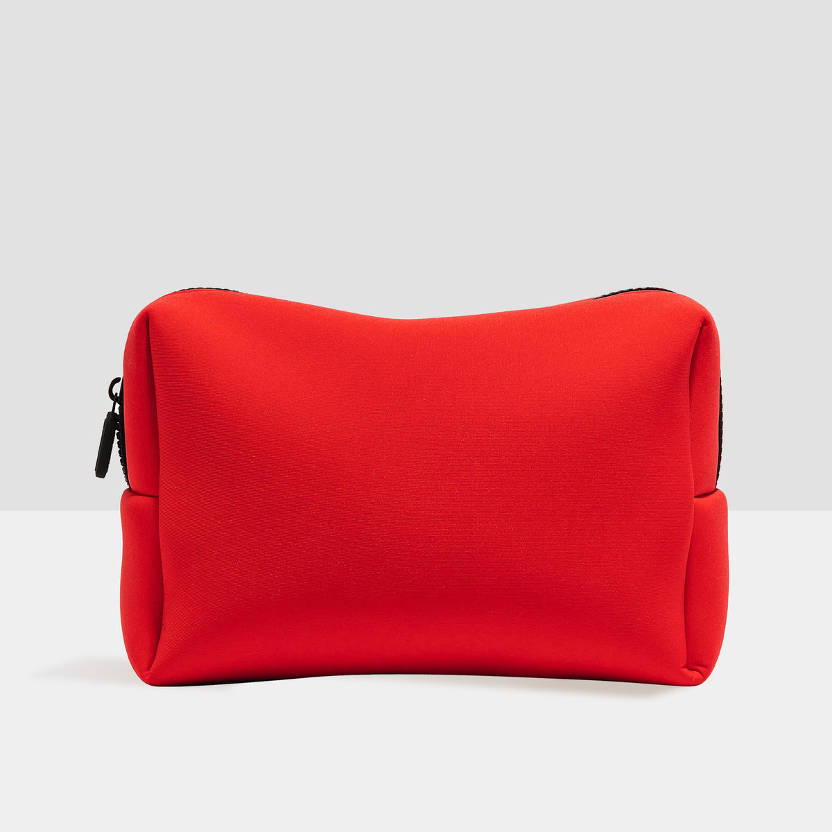 Red travel bag with rounded shape, dark zipper trim, and side zipper pull.