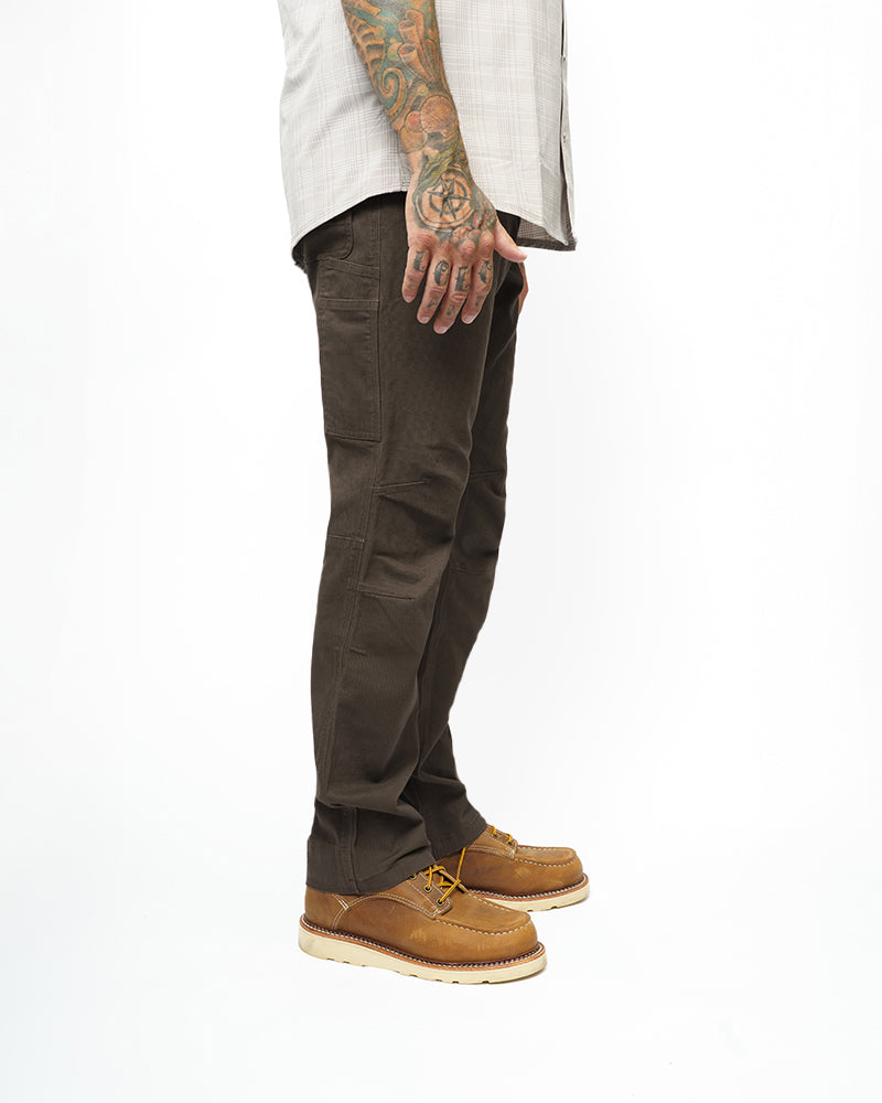 Dark brown taper-fit pants leg close-up with cargo pocket and stitched knee panel.
