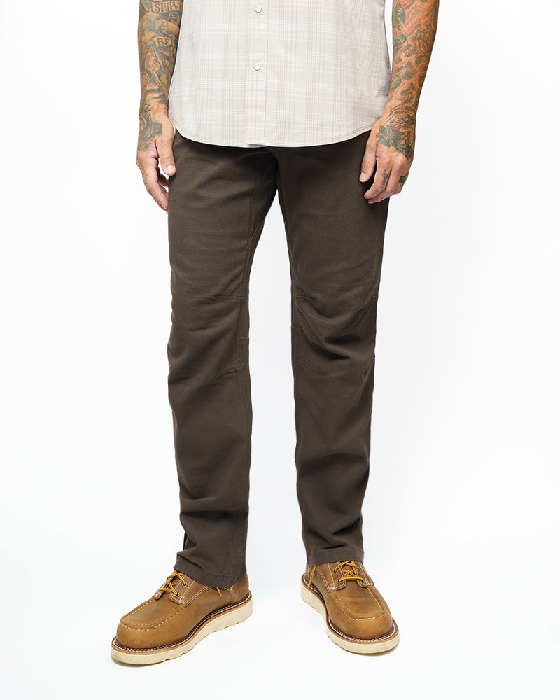 Dark brown taper-fit pants on model, full-length view with tapered legs and front pockets.