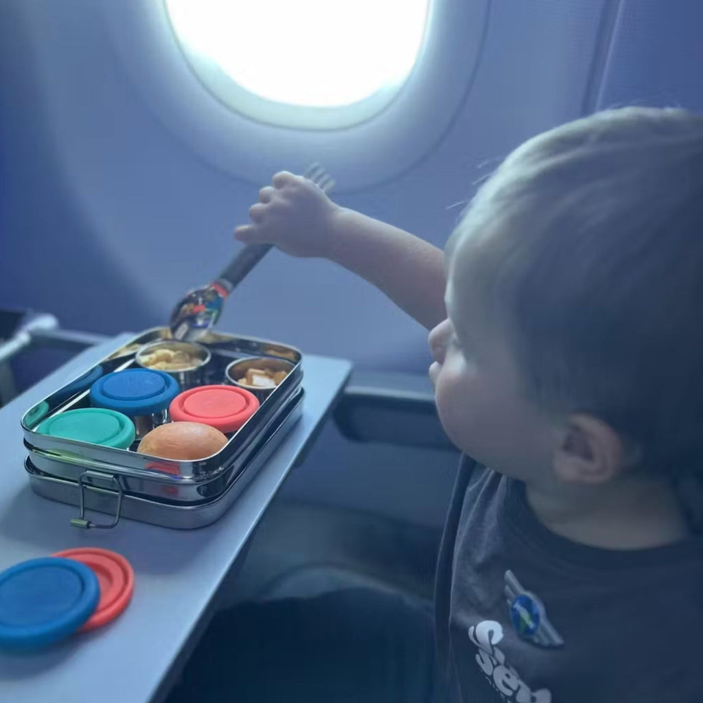 Stainless steel bento snack box on tray table with colored lids and divided compartments