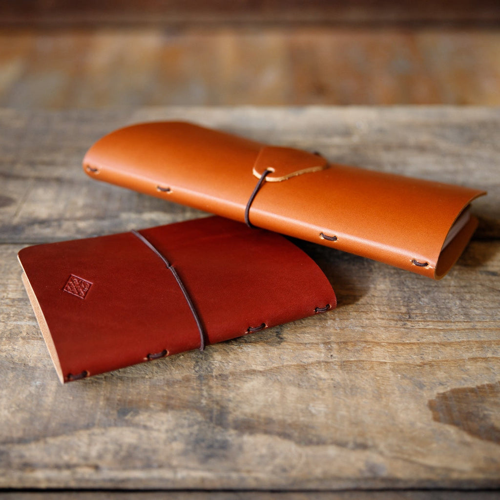 Red leather traveler notebook with strap closure, lying on wooden tabletop