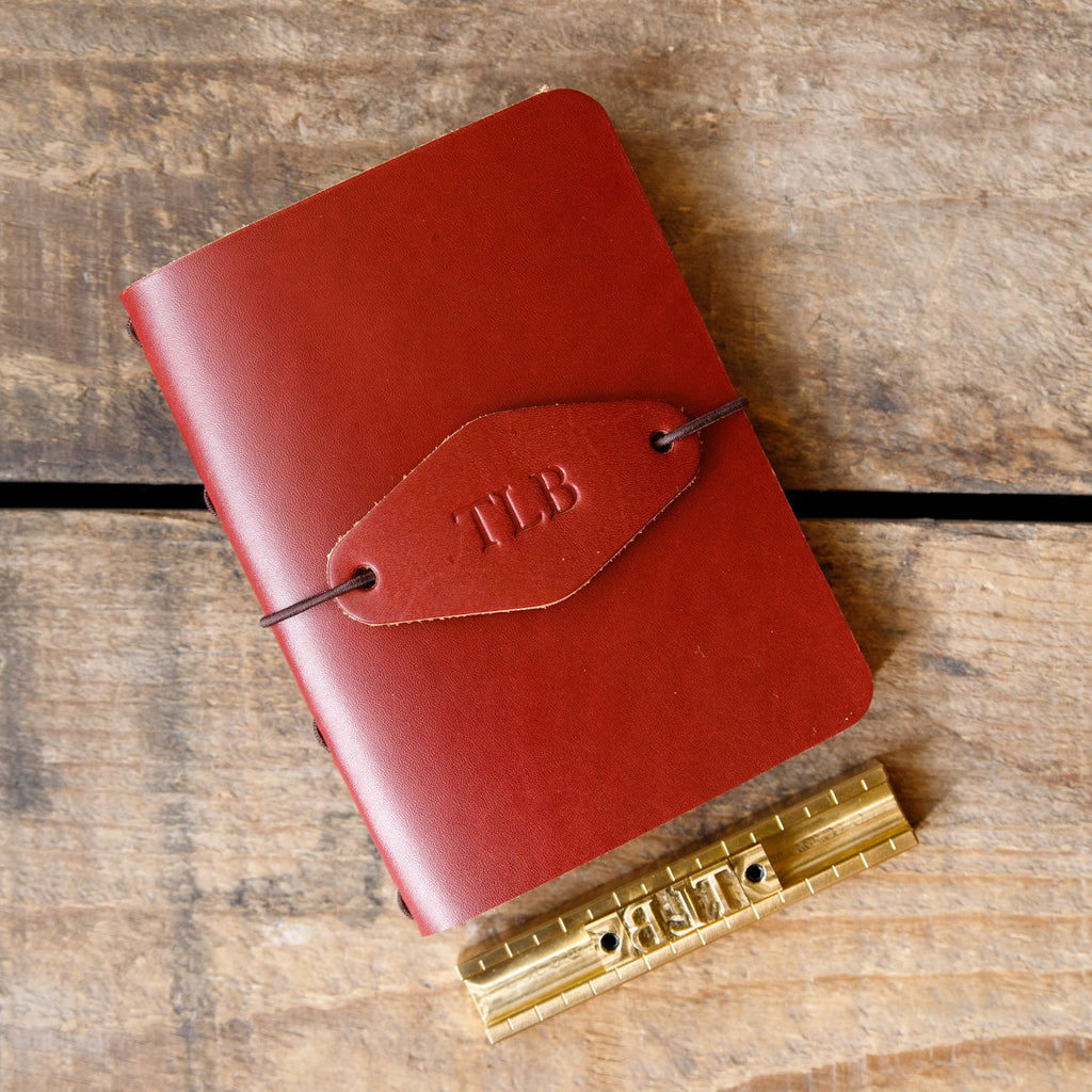Oxblood leather traveler notebook with TLB initials and strap closure, close-up