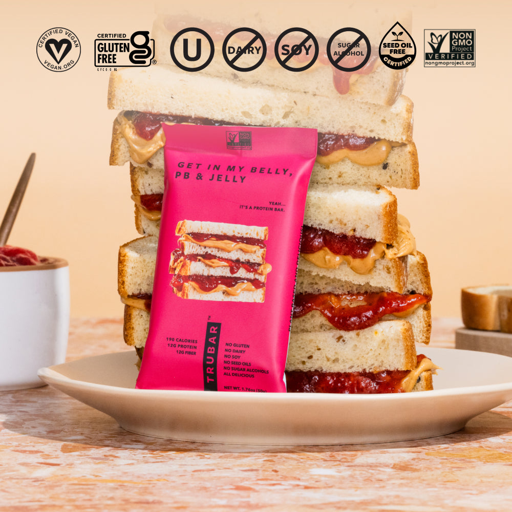 TRUBAR pink protein bar pouch in front of stacked sandwich slices