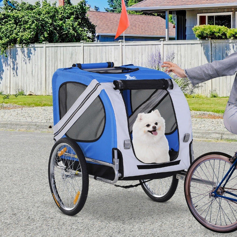 Blue pet bike trailer with small dog in front compartment window and safety flag