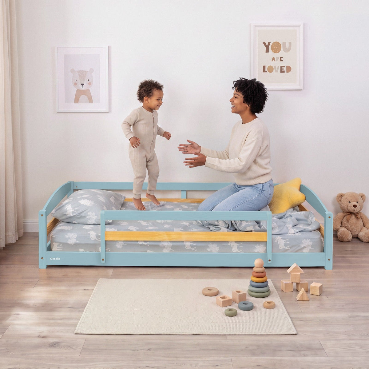 Blue twin floor bed with safety guardrails and patterned bedding; child standing beside it