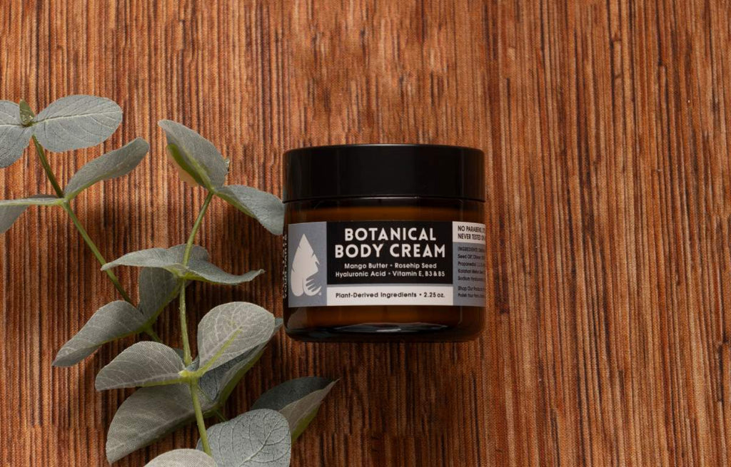 Botanical body cream jar with leafy greens beside it