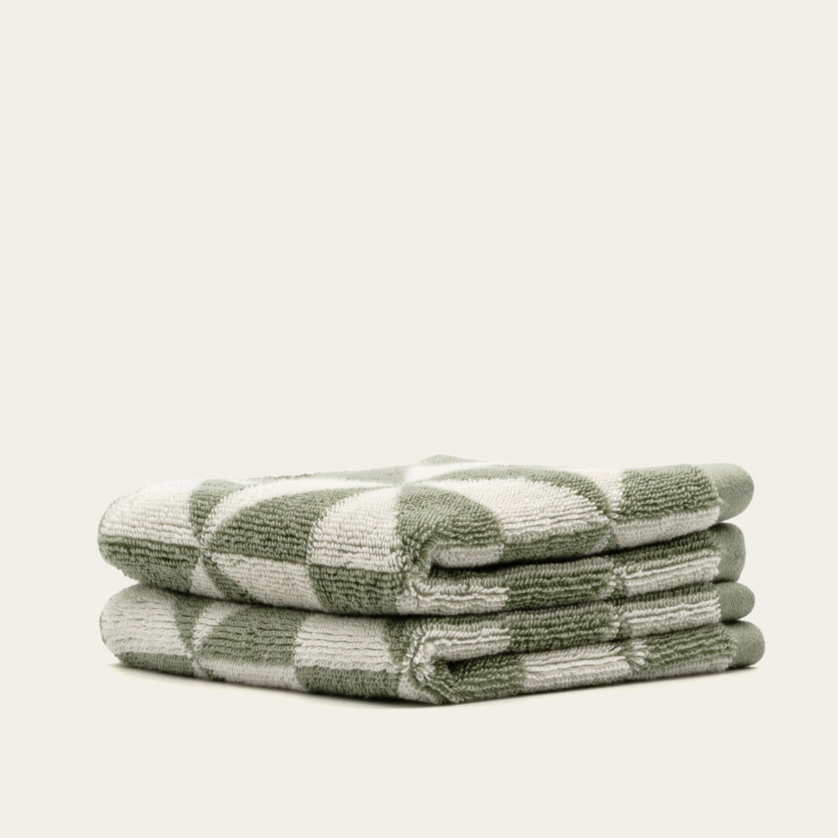 Sage and ecru geometric cotton towels, angled stack with terry texture clearly visible.