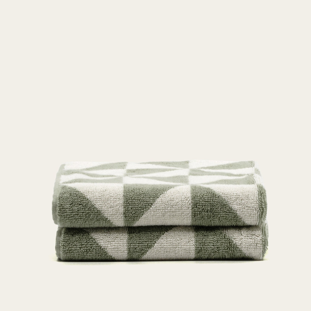 Sage and ecru geometric cotton towels, stacked in two layers with soft terry loops.