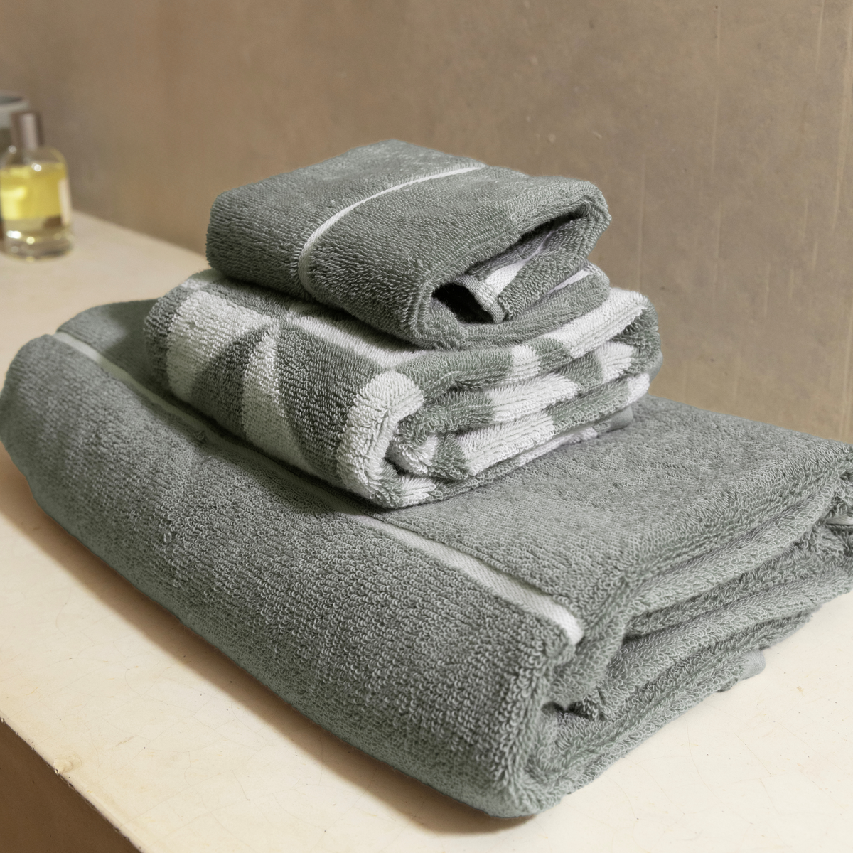Sage green cotton towel roll stack with white stripes and soft terry texture