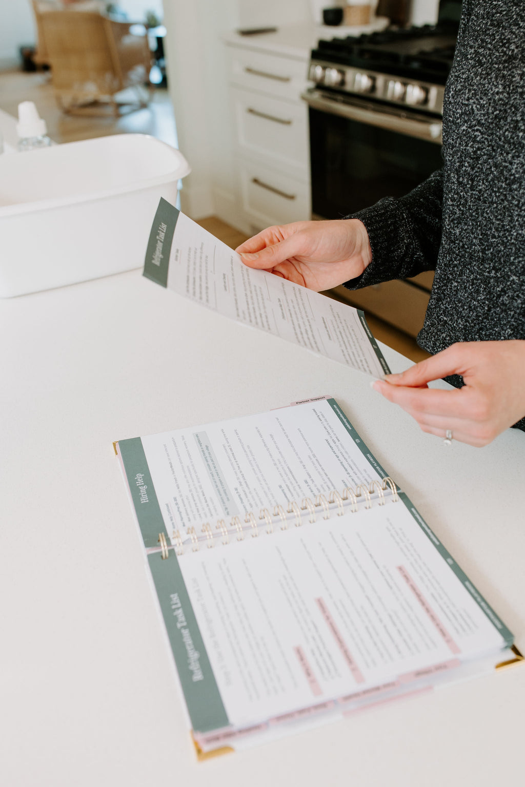 Postpartum planner guide with printed checklist pages, held open while someone writes
