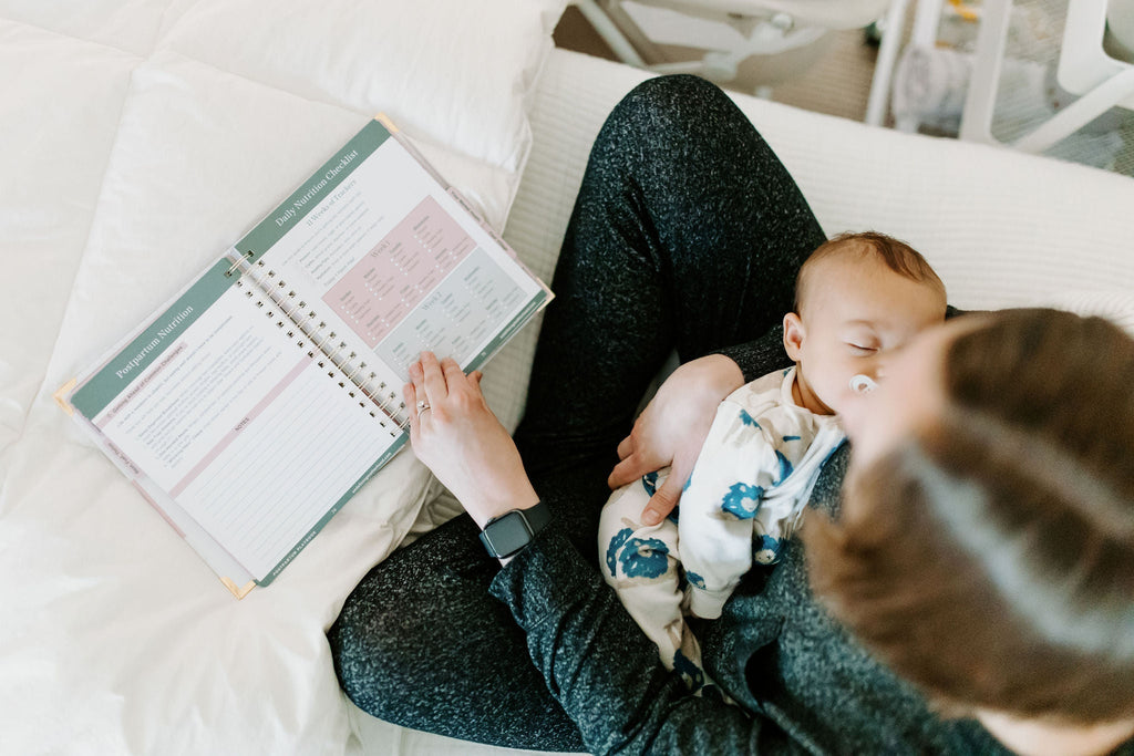 Postpartum planner open on a sofa beside a sleeping infant