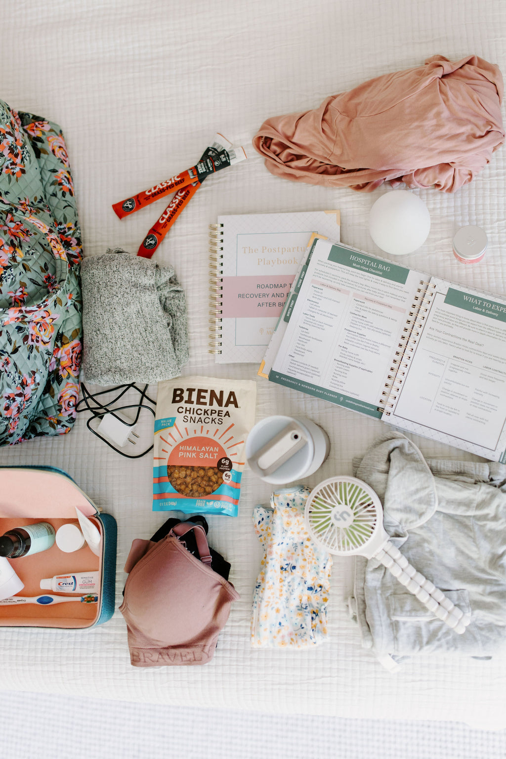 Postpartum planner guide and notebook open on a tabletop with everyday items