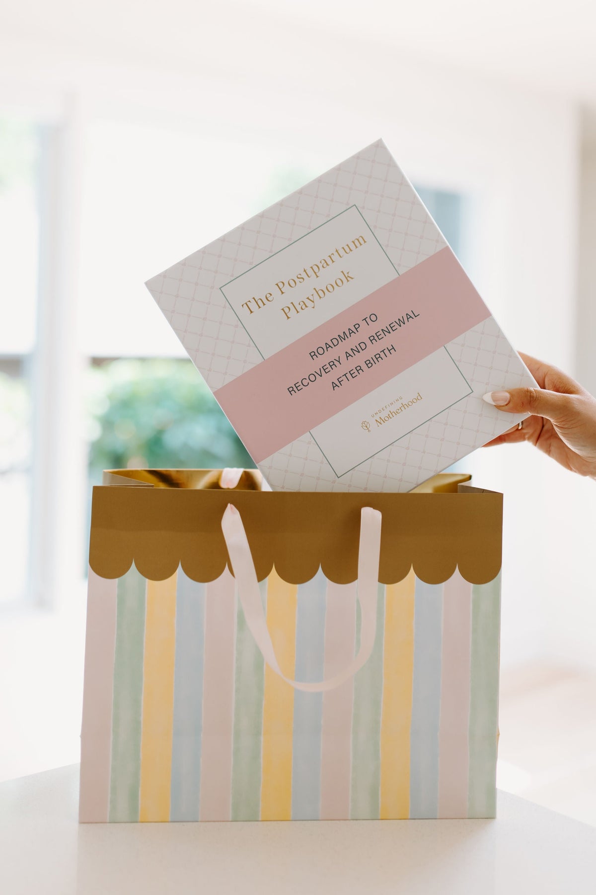 Postpartum planner guide held upright above a gift bag with decorative stripes