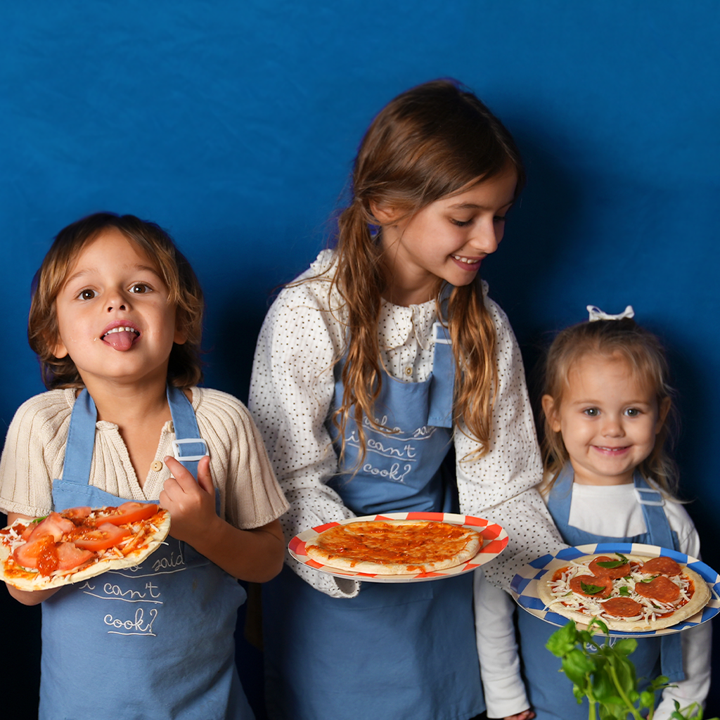 Children wearing blue chambray linen cooking aprons with embroidered script bib front