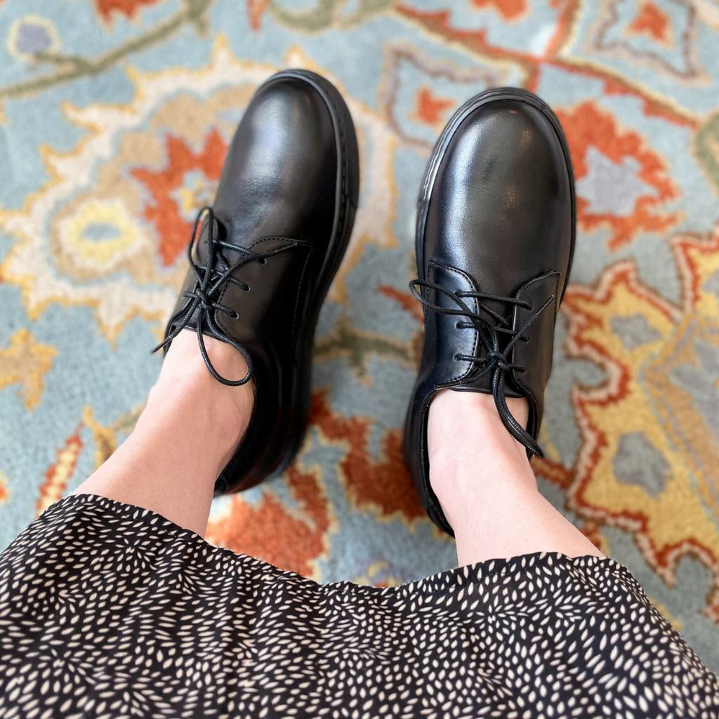 Black lace-up oxfords on feet with rounded toe and thin laces.